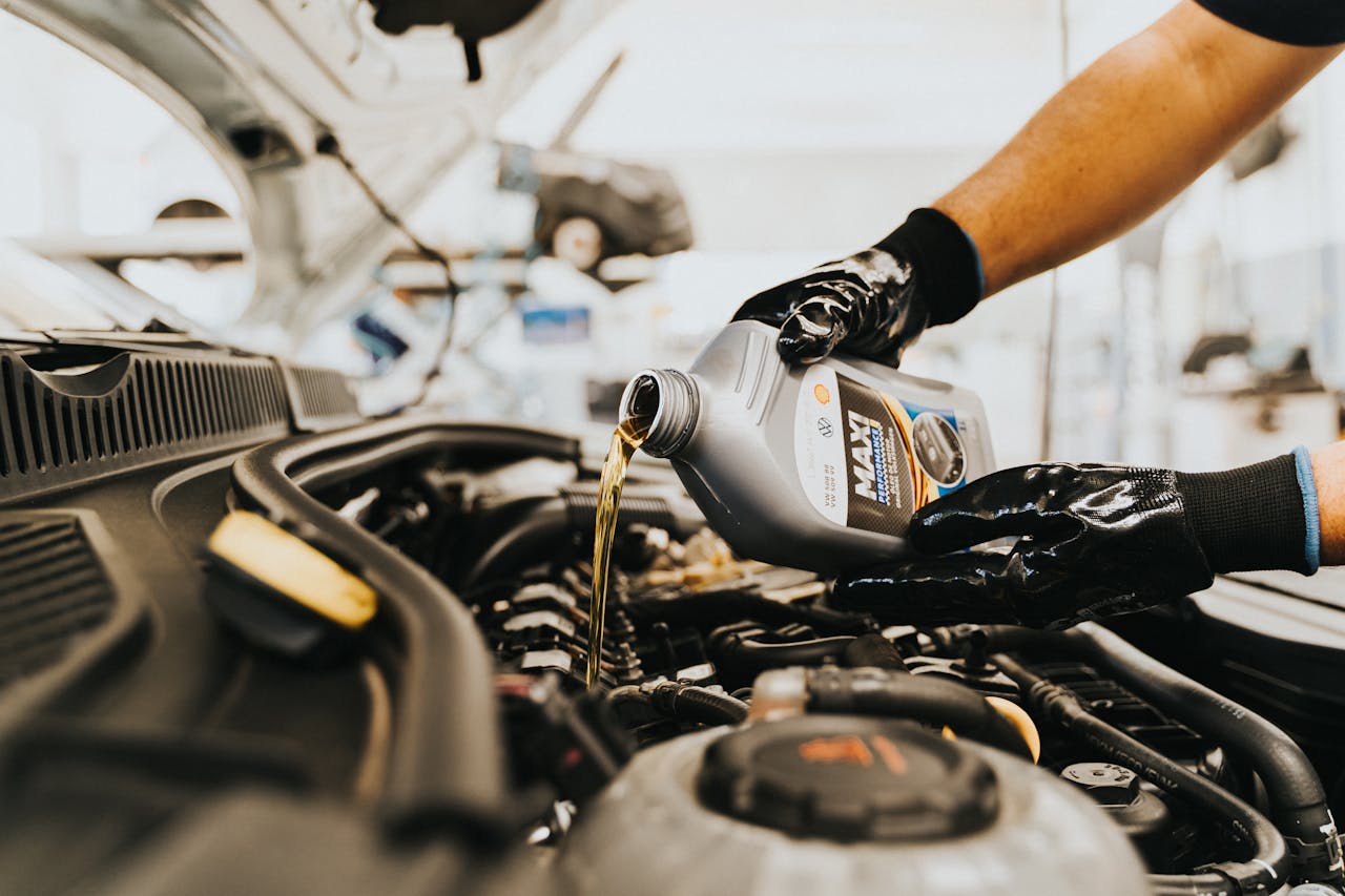 Services-03 Close-up of a mechanic pouring engine oil into a car engine in an auto repair shop.