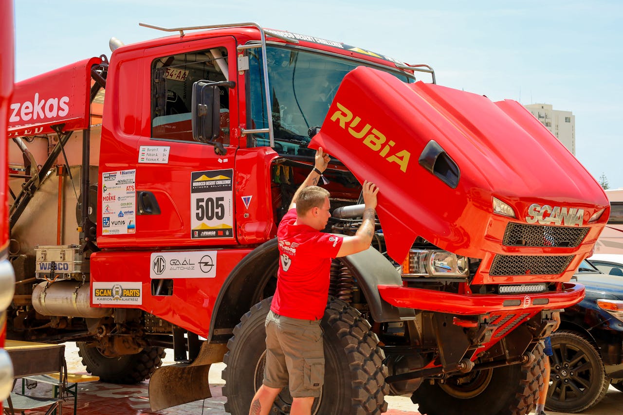 Services-02 Mechanic checking a red rally truck's engine during a desert competition event.