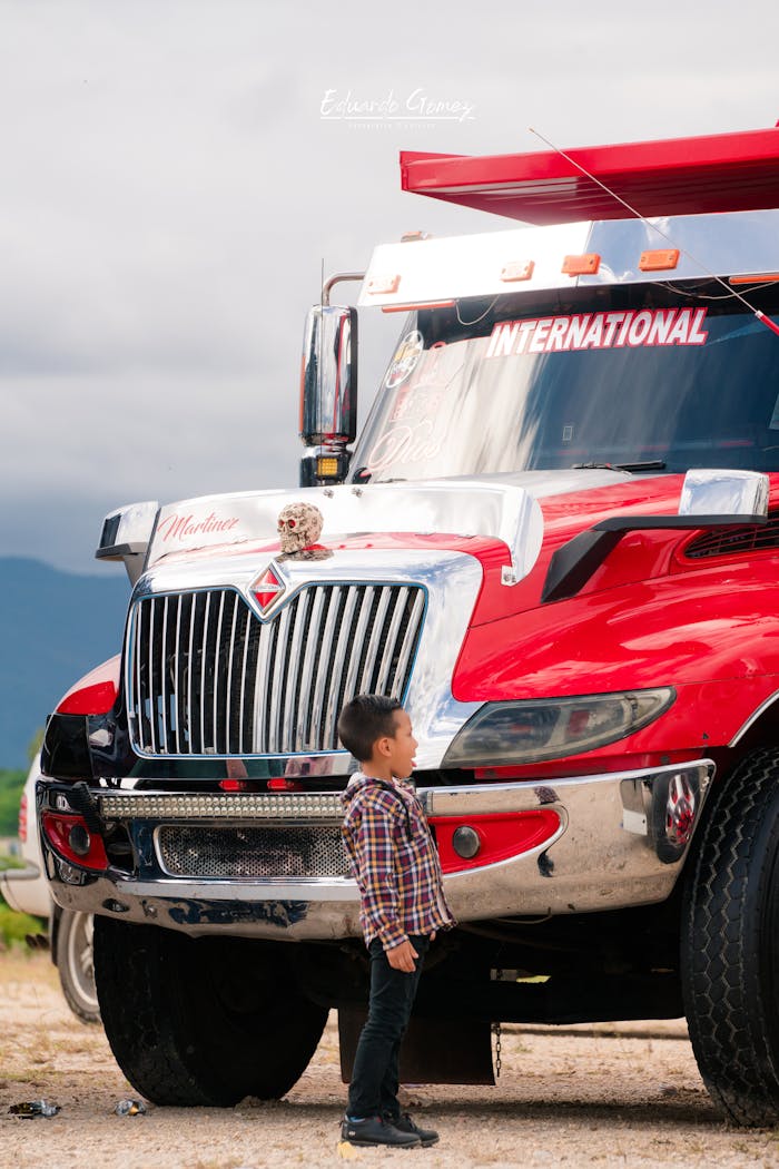 why-choose-us A young boy stands captivated by a large red semi-truck parked outdoors, showcasing vibrant contrasts.