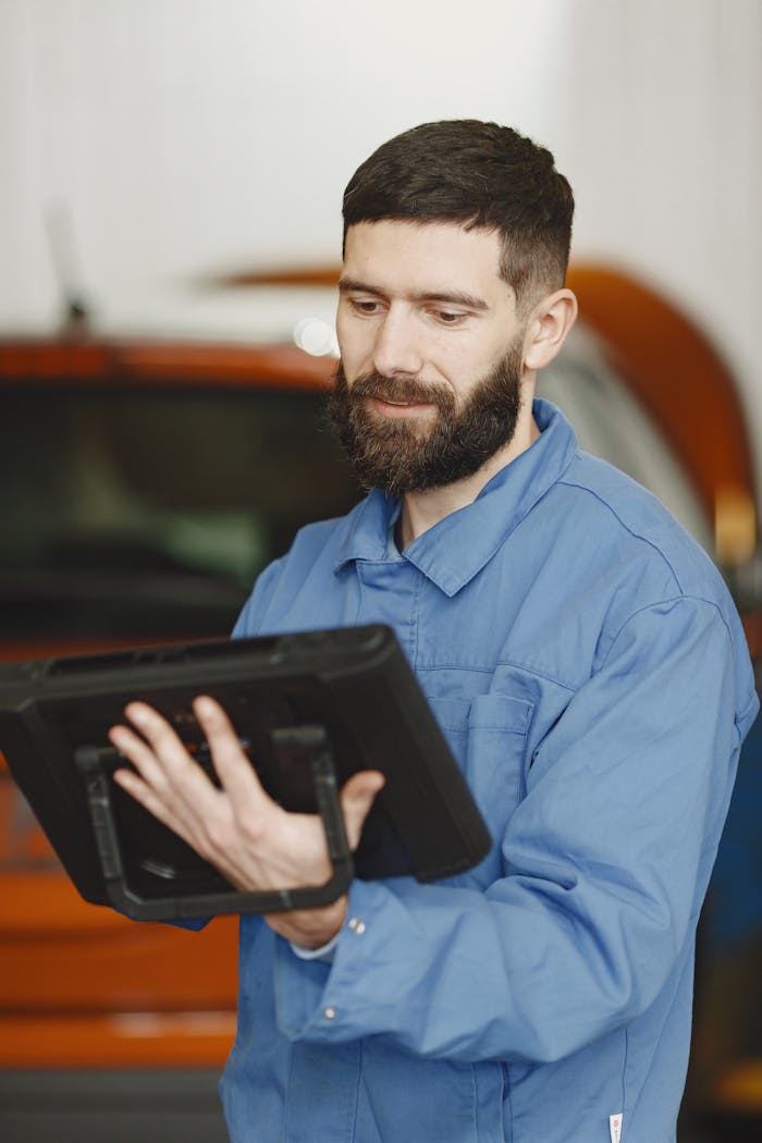 Bearded male mechanic using a tablet for diagnostics in a workshop setting.